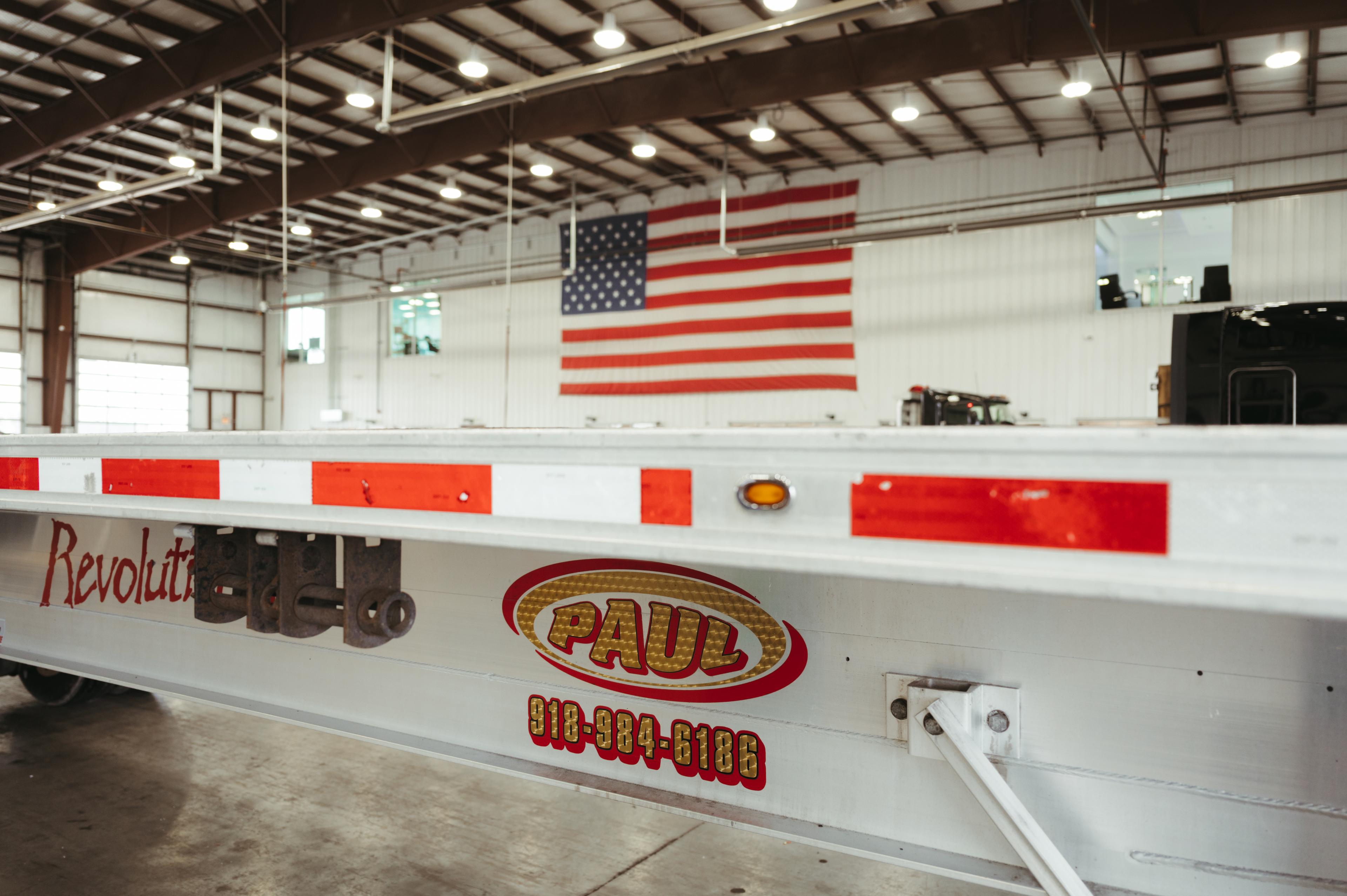 The side of a Paul flatbed trailer in the shop, with an American flag on the wall behind it.